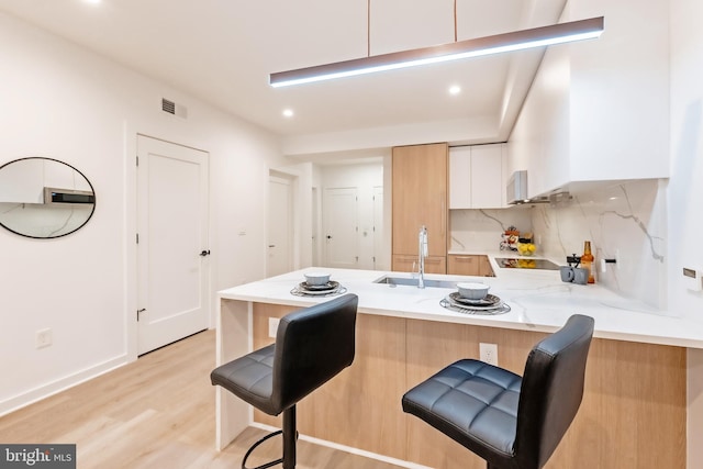 kitchen featuring white cabinets, sink, kitchen peninsula, light hardwood / wood-style flooring, and a kitchen bar