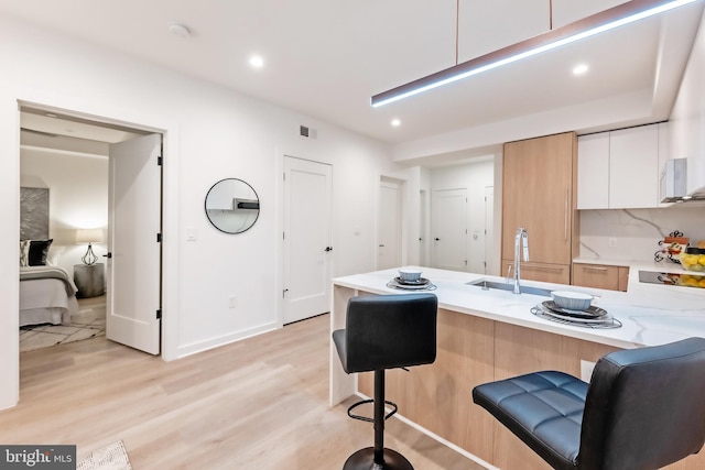 kitchen with light wood-type flooring, a breakfast bar area, sink, kitchen peninsula, and white cabinetry