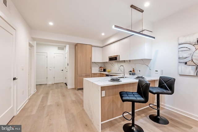 kitchen featuring white cabinets, sink, kitchen peninsula, decorative light fixtures, and a kitchen bar