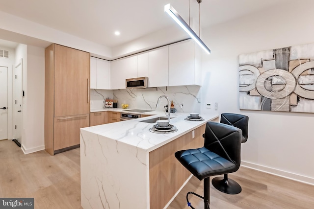 kitchen with hanging light fixtures, white cabinetry, a breakfast bar, light wood-type flooring, and decorative backsplash