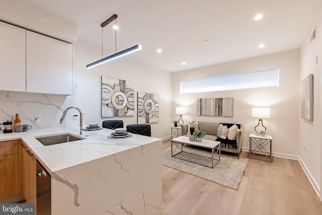 kitchen featuring light stone counters, sink, white cabinetry, light hardwood / wood-style floors, and decorative backsplash