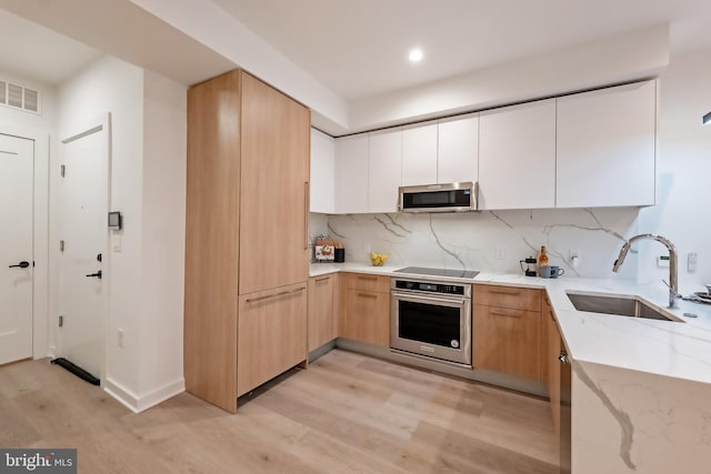 kitchen with white cabinets, light hardwood / wood-style floors, appliances with stainless steel finishes, and sink