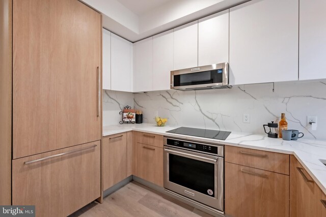 kitchen featuring light stone countertops, stainless steel appliances, light hardwood / wood-style floors, white cabinetry, and backsplash