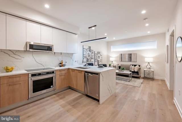 kitchen with light wood-type flooring, stainless steel appliances, sink, kitchen peninsula, and white cabinetry