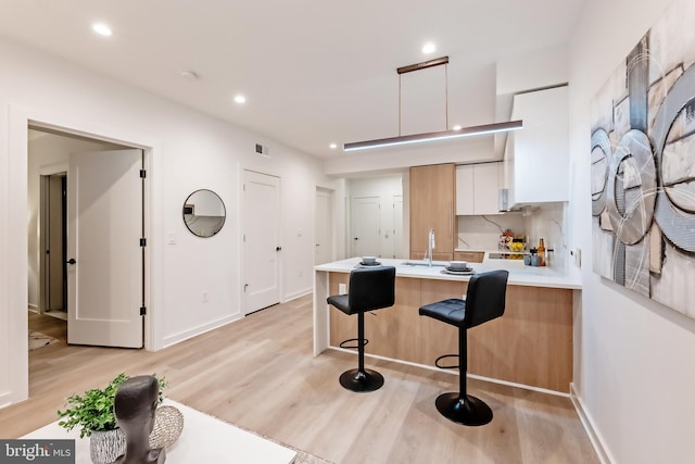 kitchen featuring kitchen peninsula, white cabinetry, a breakfast bar area, light wood-type flooring, and decorative backsplash