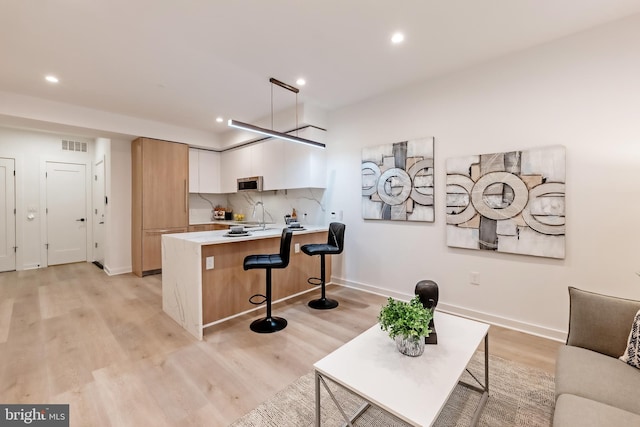 kitchen with light wood-type flooring, white cabinets, kitchen peninsula, a kitchen bar, and backsplash