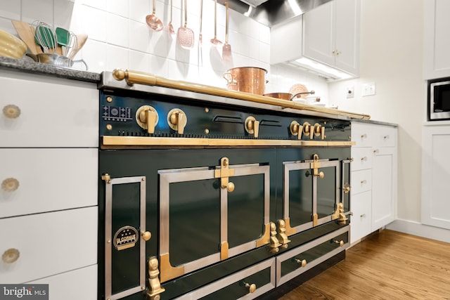 room details featuring white cabinetry, tasteful backsplash, wall chimney exhaust hood, and light wood-type flooring