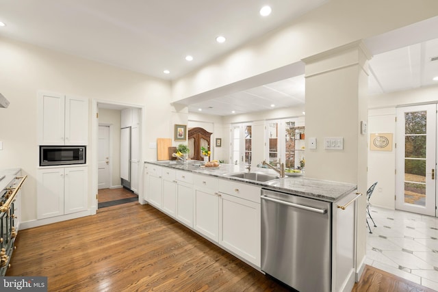 kitchen with stainless steel appliances, sink, light stone counters, a healthy amount of sunlight, and white cabinets