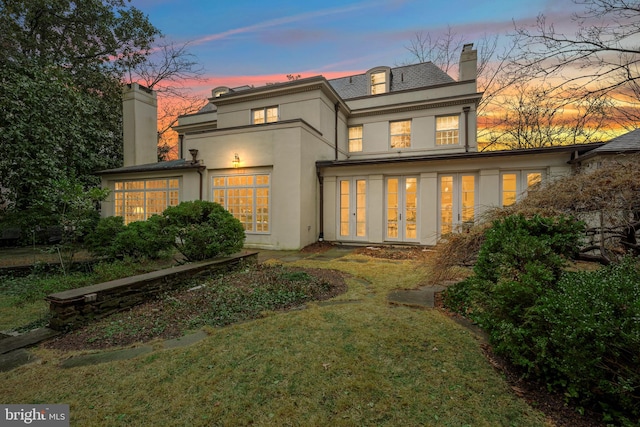 back house at dusk with a yard and french doors