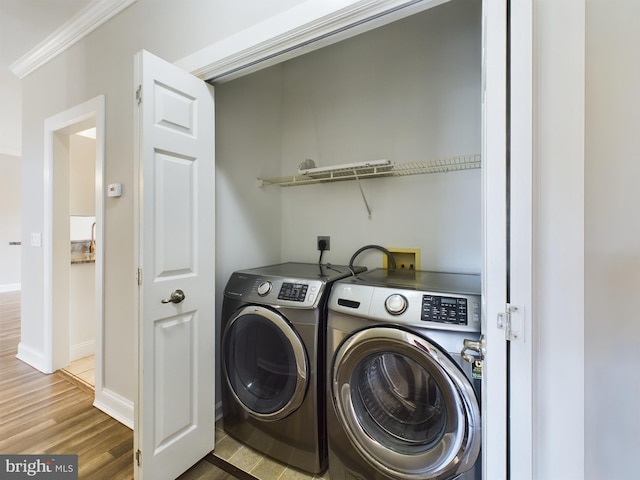 laundry area featuring wood-type flooring, ornamental molding, and washing machine and clothes dryer