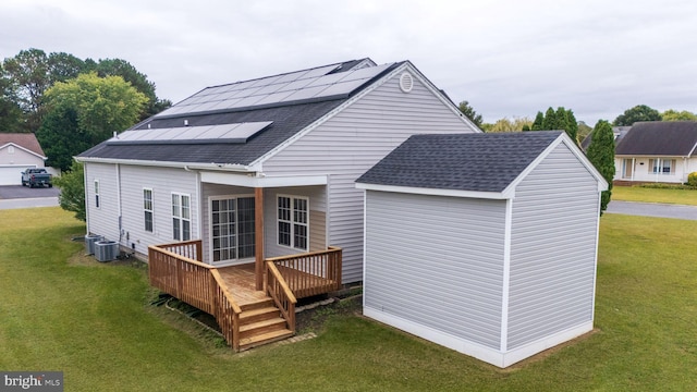 rear view of house with central AC unit, solar panels, a deck, and a lawn