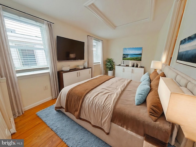 bedroom featuring multiple windows, light hardwood / wood-style flooring, and a raised ceiling