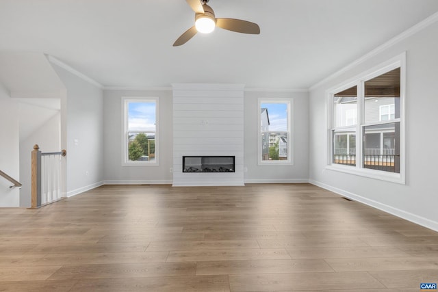 unfurnished living room featuring ornamental molding, a large fireplace, light hardwood / wood-style flooring, and ceiling fan