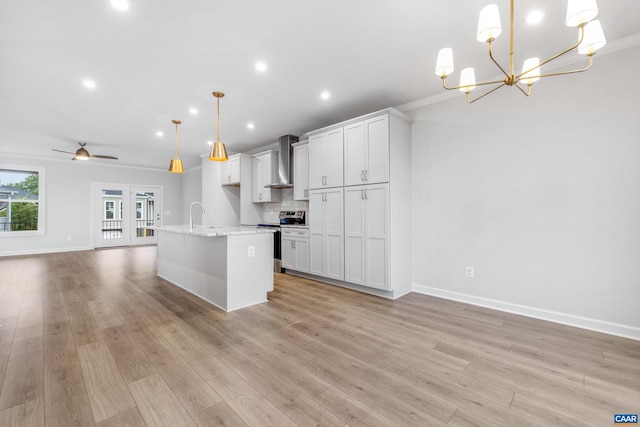 kitchen with ceiling fan with notable chandelier, decorative light fixtures, stainless steel electric range oven, a center island with sink, and wall chimney range hood