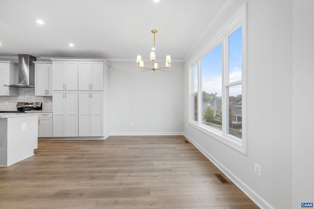 kitchen featuring white cabinets, wall chimney exhaust hood, crown molding, and light hardwood / wood-style flooring