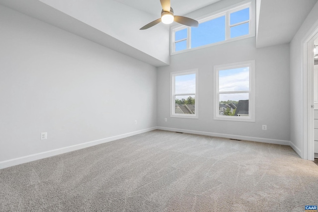 carpeted spare room with a towering ceiling and ceiling fan