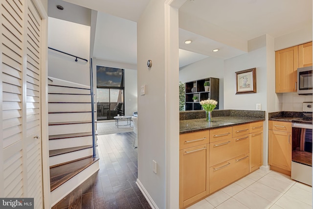 kitchen featuring light brown cabinets, light hardwood / wood-style flooring, dark stone counters, and range