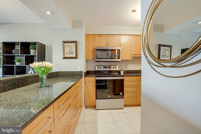 kitchen with stainless steel appliances, backsplash, dark stone counters, light tile patterned floors, and light brown cabinetry