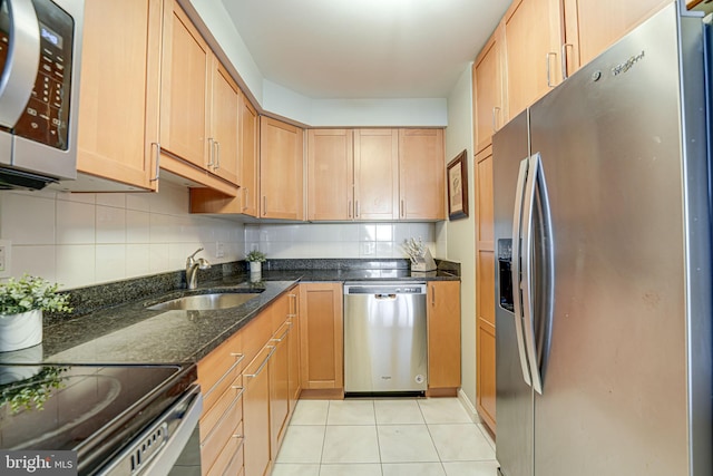 kitchen with sink, stainless steel appliances, dark stone counters, decorative backsplash, and light tile patterned floors