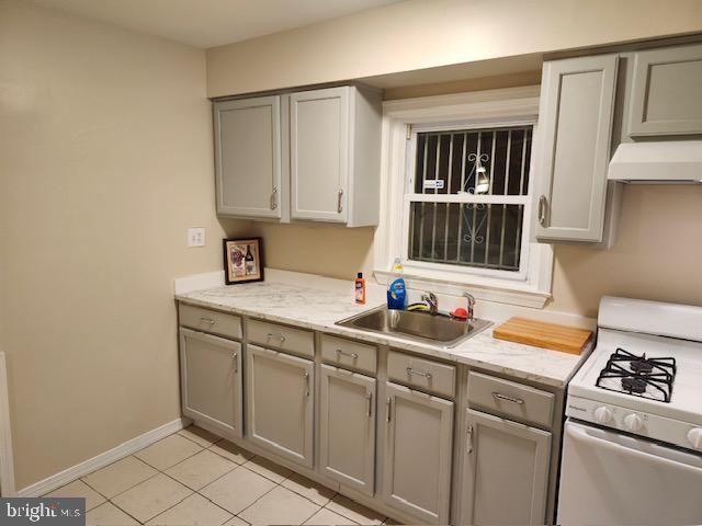 kitchen featuring gray cabinetry, gas range gas stove, light tile patterned floors, custom exhaust hood, and sink