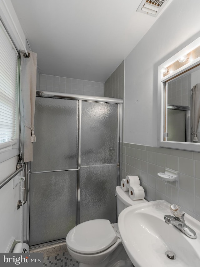 bathroom featuring tile walls, a shower with door, toilet, and sink