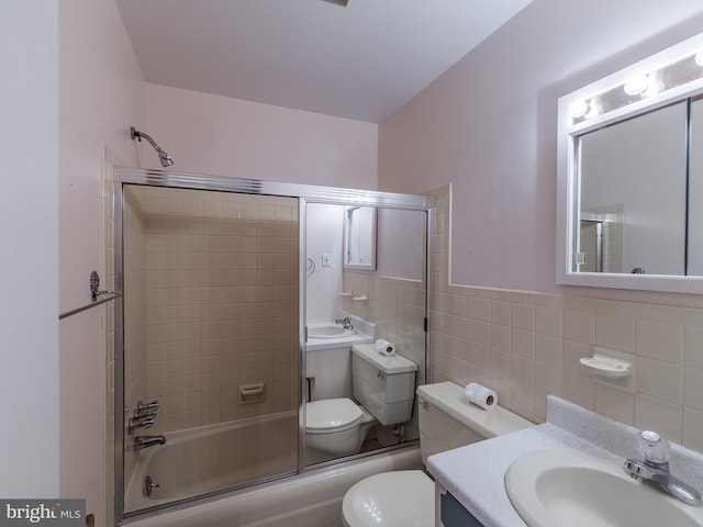 full bathroom featuring enclosed tub / shower combo, vanity, tile walls, and toilet