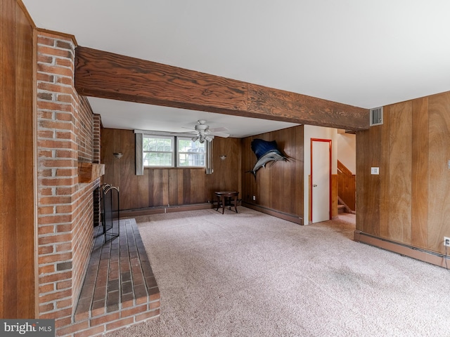 unfurnished living room featuring carpet flooring, wooden walls, ceiling fan, and a brick fireplace