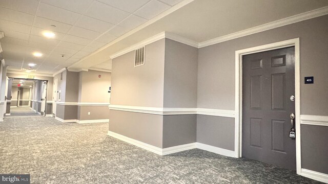 carpeted empty room featuring crown molding and a drop ceiling