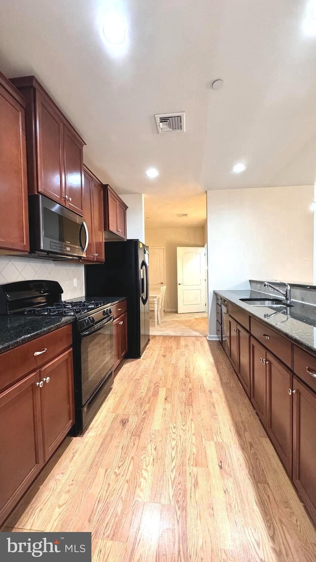 kitchen featuring dark stone counters, black appliances, sink, light wood-type flooring, and tasteful backsplash