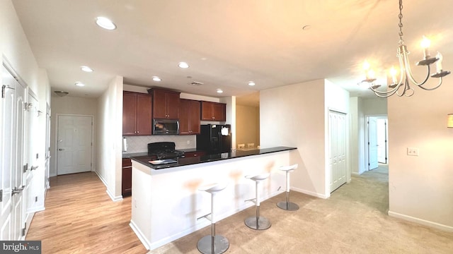 kitchen featuring an inviting chandelier, kitchen peninsula, decorative light fixtures, light carpet, and black appliances