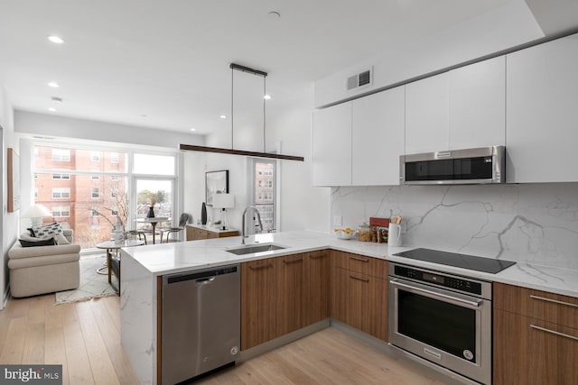 kitchen featuring appliances with stainless steel finishes, white cabinetry, kitchen peninsula, light hardwood / wood-style flooring, and sink