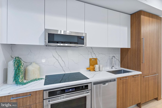 kitchen featuring sink, white cabinets, decorative backsplash, appliances with stainless steel finishes, and light stone countertops