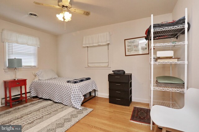 bedroom with a baseboard heating unit, ceiling fan, and hardwood / wood-style flooring