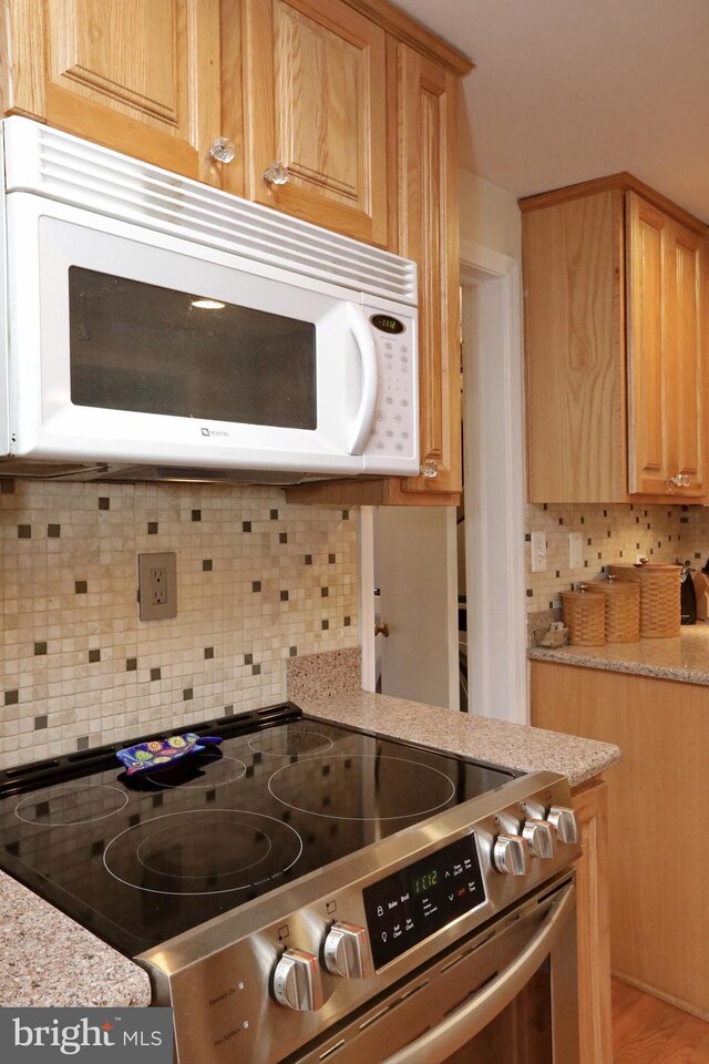 kitchen featuring light wood-type flooring, stainless steel range oven, and backsplash