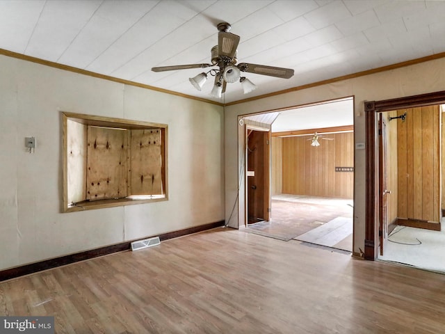 empty room featuring crown molding, wooden walls, hardwood / wood-style floors, and ceiling fan