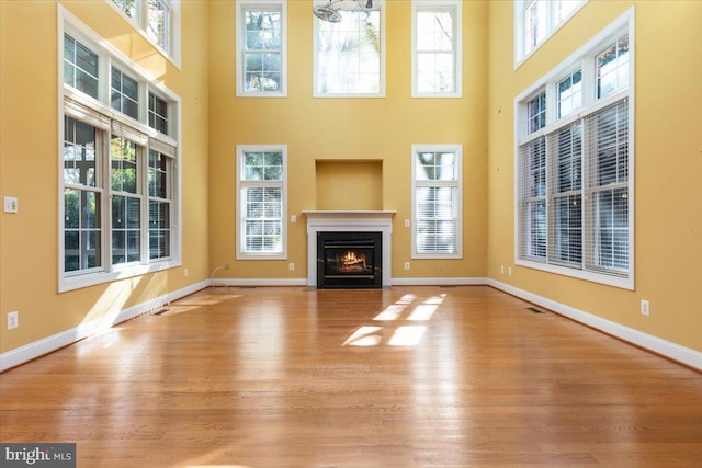 unfurnished living room featuring light hardwood / wood-style floors, plenty of natural light, and a towering ceiling