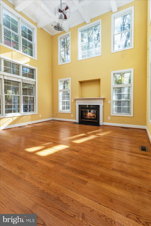 unfurnished living room with hardwood / wood-style floors, a healthy amount of sunlight, and beam ceiling