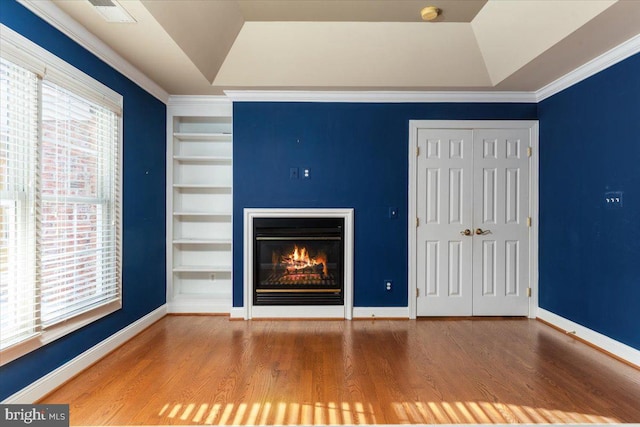 unfurnished living room with hardwood / wood-style flooring, built in features, a tray ceiling, and ornamental molding