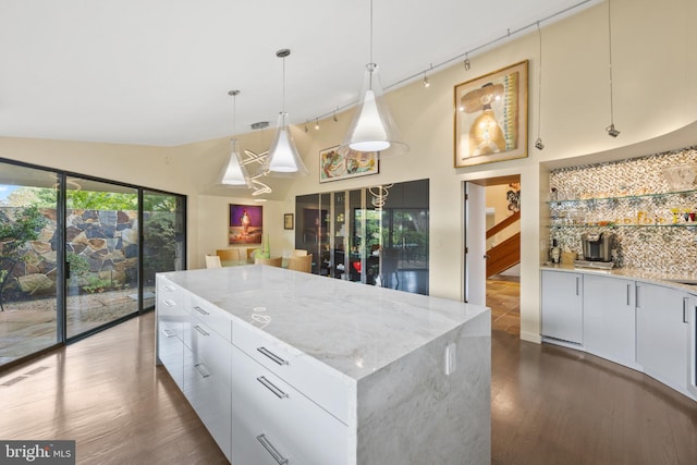 kitchen with light stone counters, vaulted ceiling, decorative light fixtures, white cabinets, and a large island