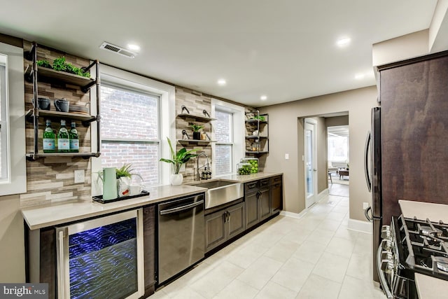 kitchen featuring dark brown cabinets, sink, beverage cooler, decorative backsplash, and appliances with stainless steel finishes