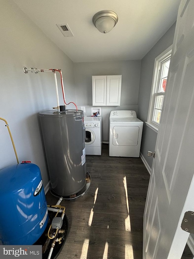 clothes washing area with water heater, dark wood-style flooring, washing machine and clothes dryer, visible vents, and cabinet space