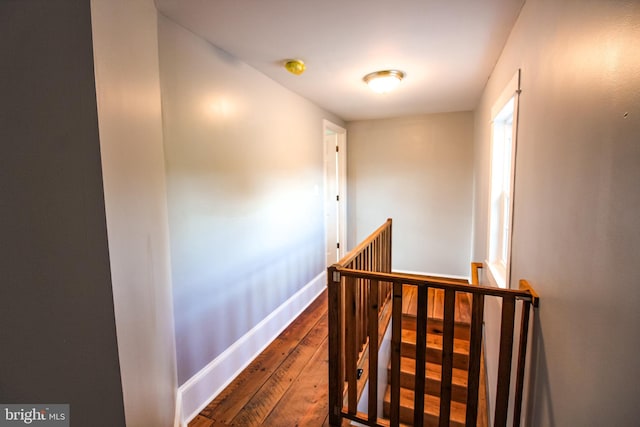 hall featuring baseboards, dark wood-style floors, and an upstairs landing