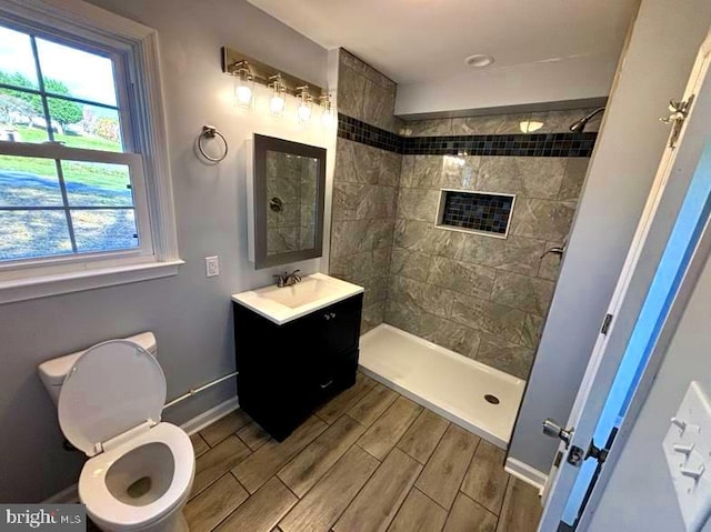 bathroom featuring vanity, a tile shower, toilet, baseboards, and wood tiled floor