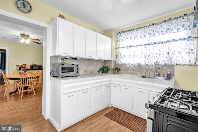 kitchen with white cabinetry, sink, gas stove, backsplash, and light hardwood / wood-style flooring