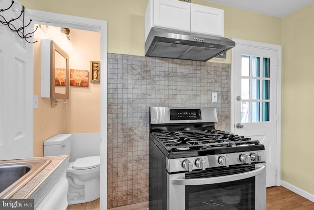 kitchen with white cabinetry, light wood-type flooring, exhaust hood, tile countertops, and stainless steel range with gas stovetop