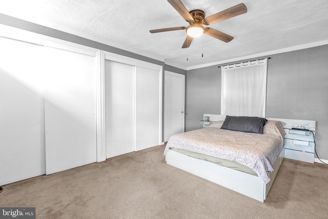 bedroom with ceiling fan, light colored carpet, a textured ceiling, and multiple closets