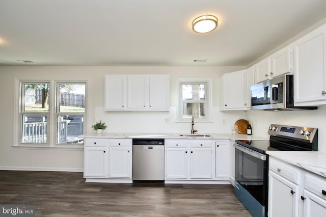 kitchen with dark wood-type flooring, white cabinets, sink, light stone countertops, and appliances with stainless steel finishes