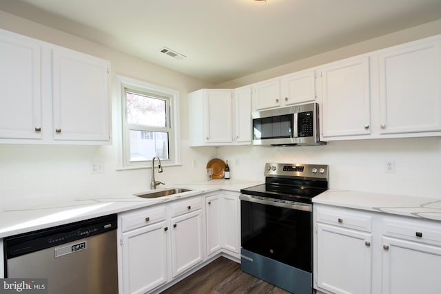 kitchen with sink, dark hardwood / wood-style floors, light stone countertops, appliances with stainless steel finishes, and white cabinetry