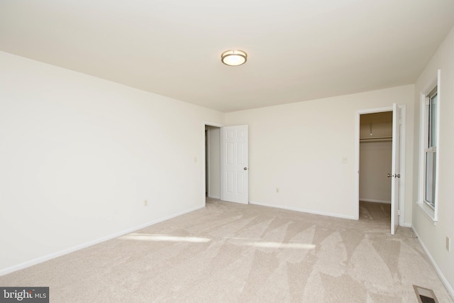 unfurnished bedroom with a walk in closet, a closet, and light colored carpet