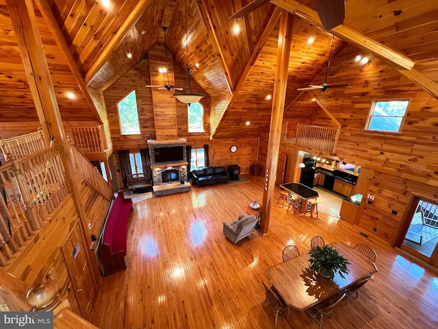 unfurnished living room featuring ceiling fan, wood walls, wood-type flooring, and high vaulted ceiling